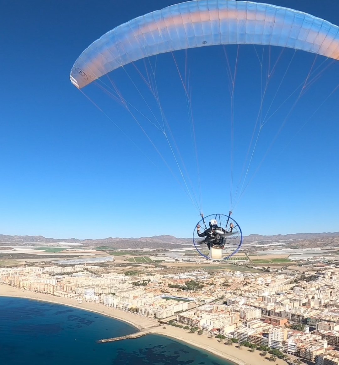 Paramotor volando sobre el pueblo y la playa